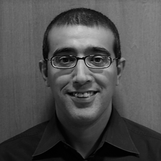 Man smiling, wearing glasses and dark shirt.